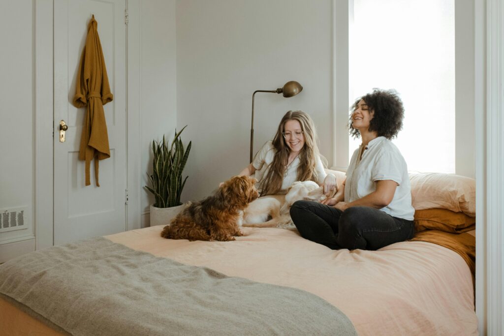 Two women and a small brown dog sitting on a bed in a pet-friendly rental property